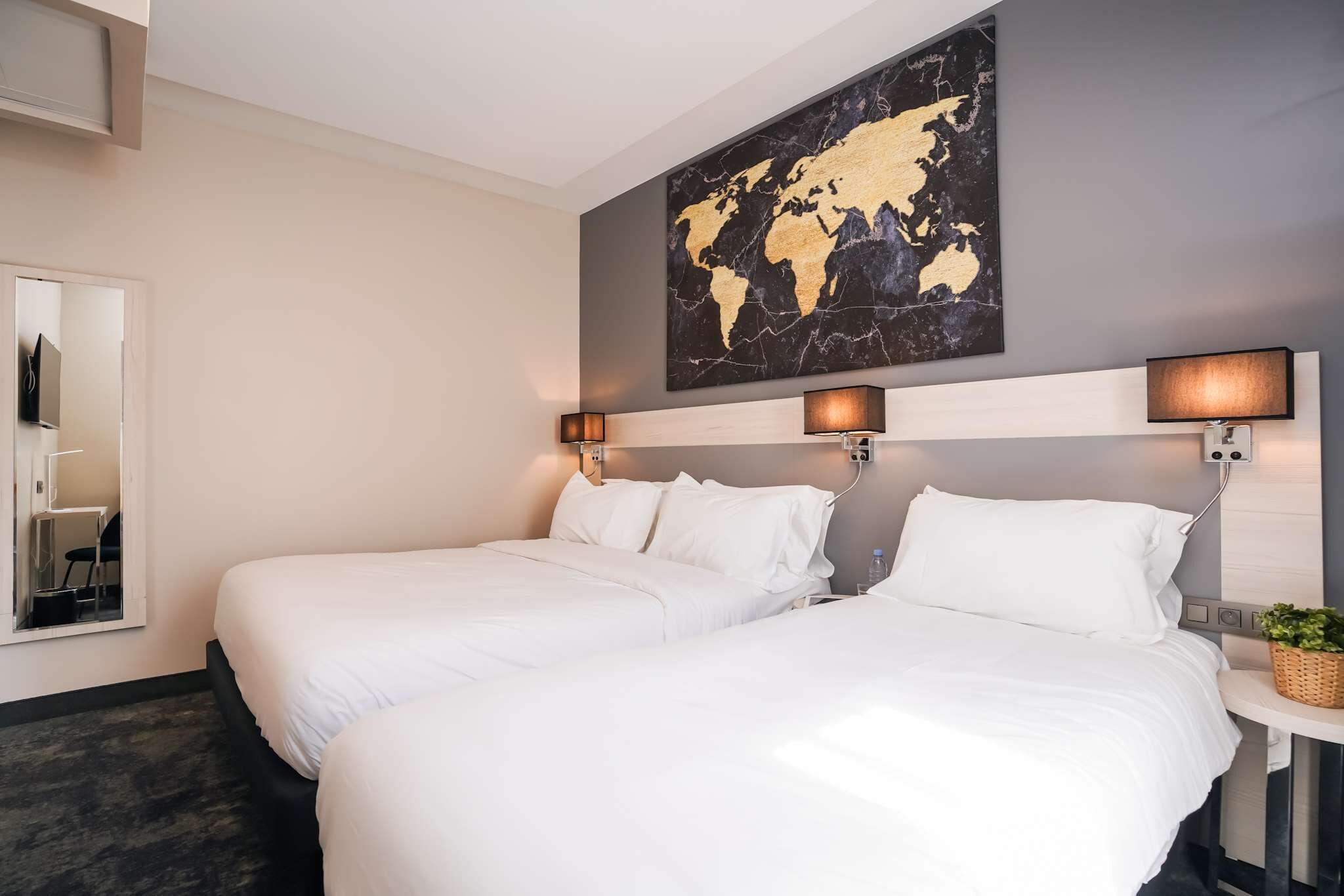 Una habitación de hotel con dos camas, un cuadro con un mapa mundial en la pared y lámparas de noche.