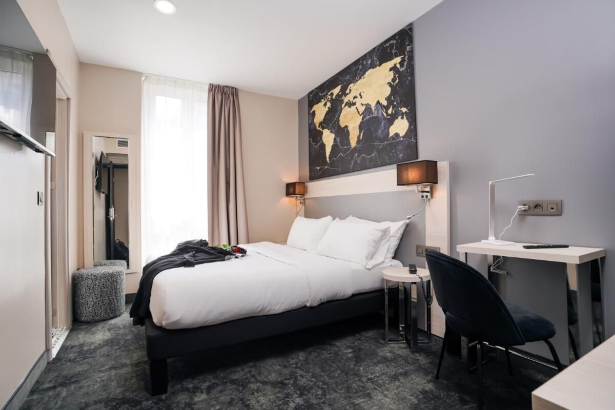 Habitación de hotel con cama, escritorio, silla, mapa mundial en la pared y ventana con cortinas.