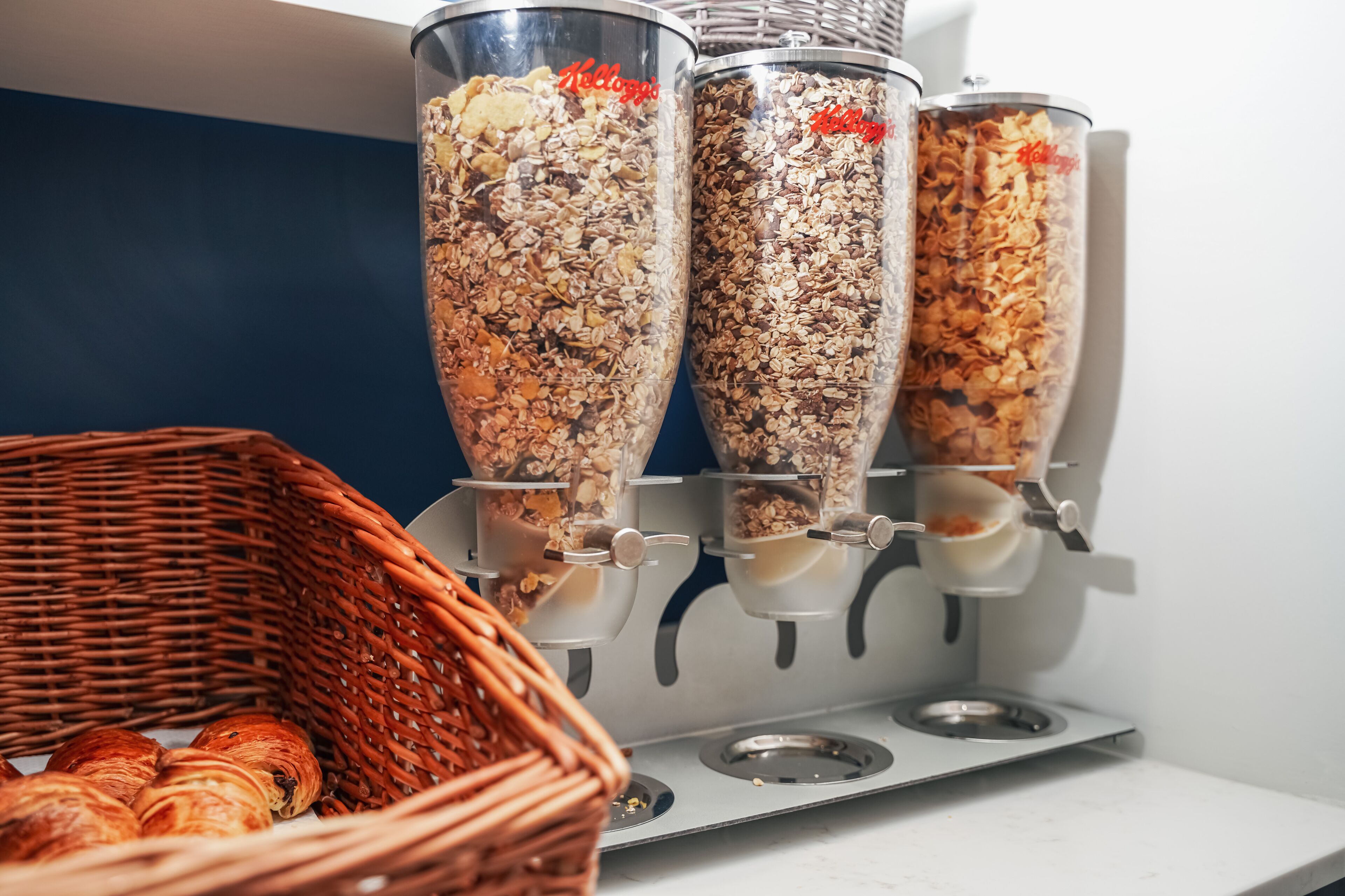 Eine Speisenausgabestation mit drei Spendern, gefüllt mit Granola, und einem Korbkörbchen mit Gebäck.
