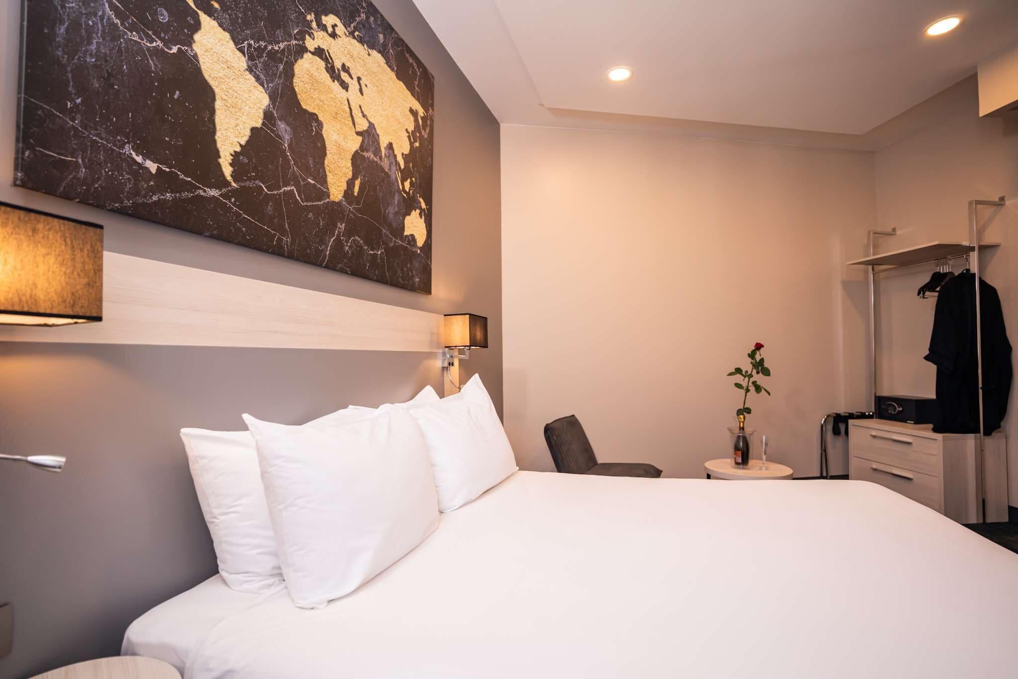 A hotel room with a large bed, a desk with a chair, a dresser, a mirror, and a map artwork on the wall.