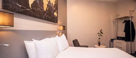 A hotel room with a large bed, a desk with a chair, a dresser, a mirror, and a map artwork on the wall.