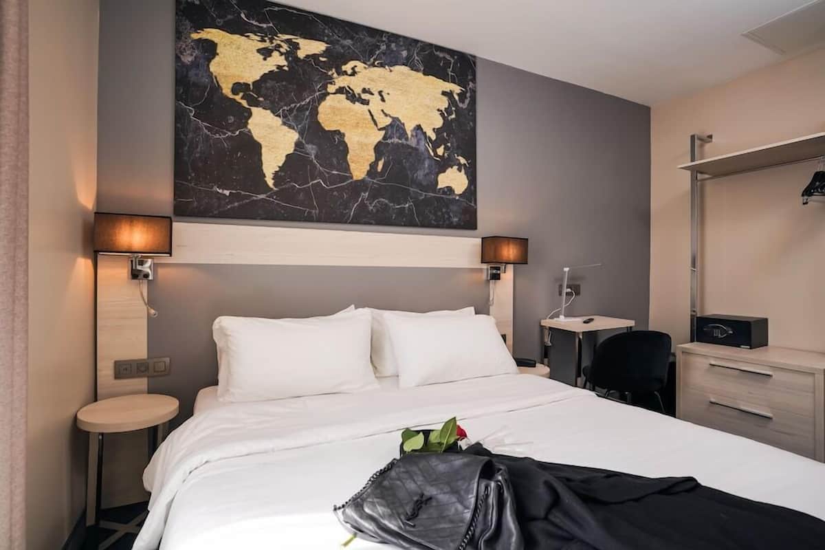 Habitación de hotel con una cama grande, dos mesitas de noche, un escritorio, una silla, un armario y un mapa del mundo en la pared.