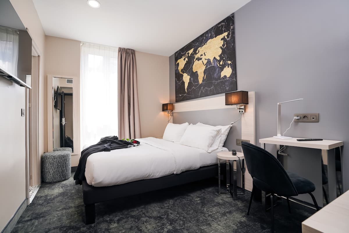 Habitación de hotel con cama, escritorio, silla, mapa mundial en la pared y ventana con cortinas.