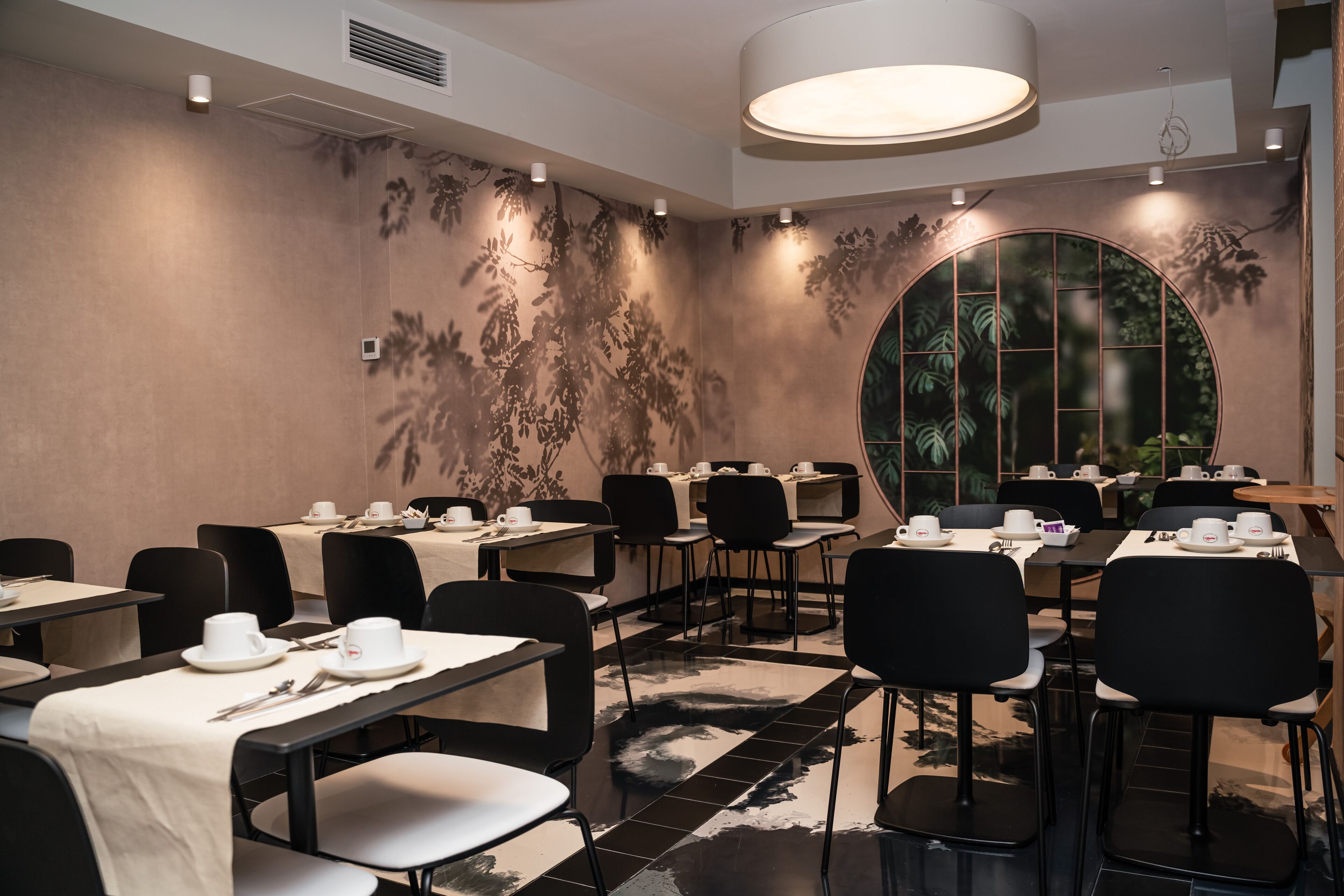 Un salón de conferencias con mesas dispuestas para reuniones, equipado con sillas y mesas, y un amplio ventanal circular con vistas a zonas verdes.
