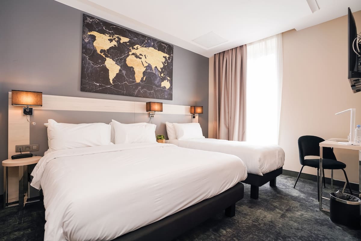 Habitación de hotel con dos camas, un escritorio, una silla, un televisor y un mapa del mundo en la pared.