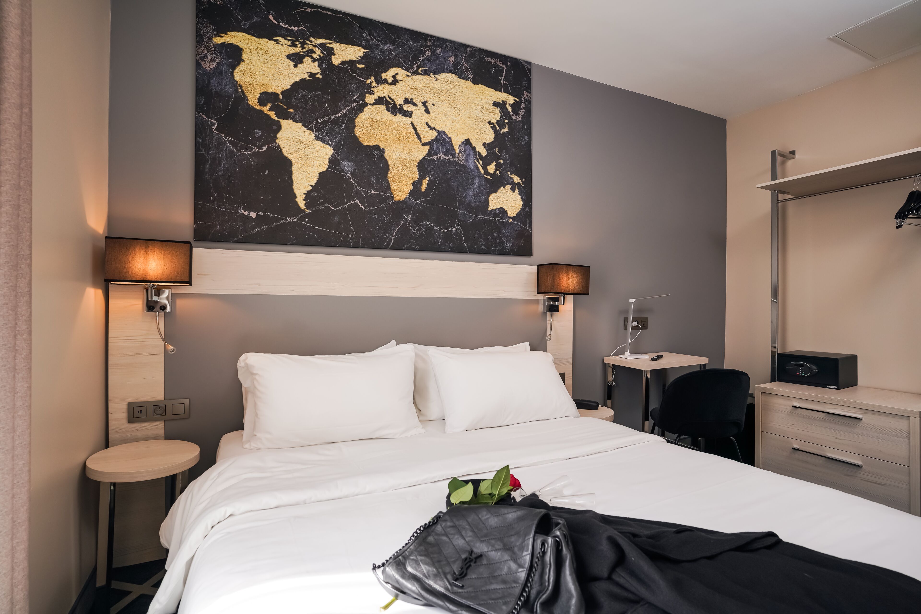 Una habitación de hotel con una cama grande, dos mesitas de noche, un escritorio, una silla, un armario y un mapa mundial en la pared.