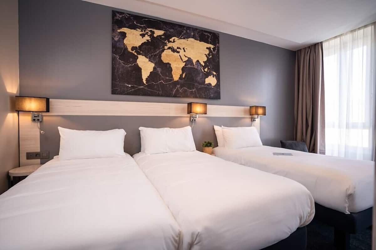 Habitación de hotel con dos camas, un cuadro de un mapa mundial en la pared y un ventanal con cortinas.