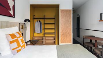 Una camera d'albergo con un letto, una scrivania, una sedia, un armadio e un appendiabiti.