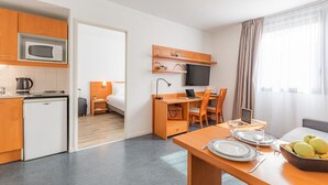 A compact hotel room with a kitchenette, a dining area, a bed, and a TV. - Appart’City Confort Lyon Gerland (Lyon)
