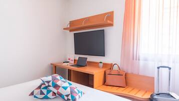 Una camera d'albergo con un letto, una scrivania con un portatile, una televisione, una valigia e una borsa.