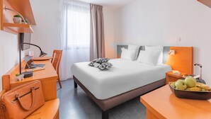 A hotel room with a bed, desk, chair, and a small table with fruit. - Appart’City Confort Lyon Gerland (Lyon)