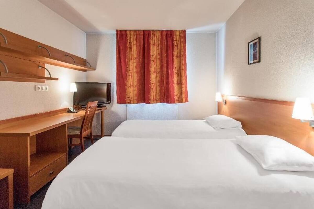 A hotel room with a bed, a desk, a chair, a television, and a window with curtains.