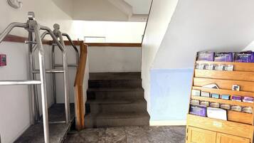 Una escalera con barandillas metálicas, un detector de incendios y un expositor de madera con guías para visitantes y cajas de vino.