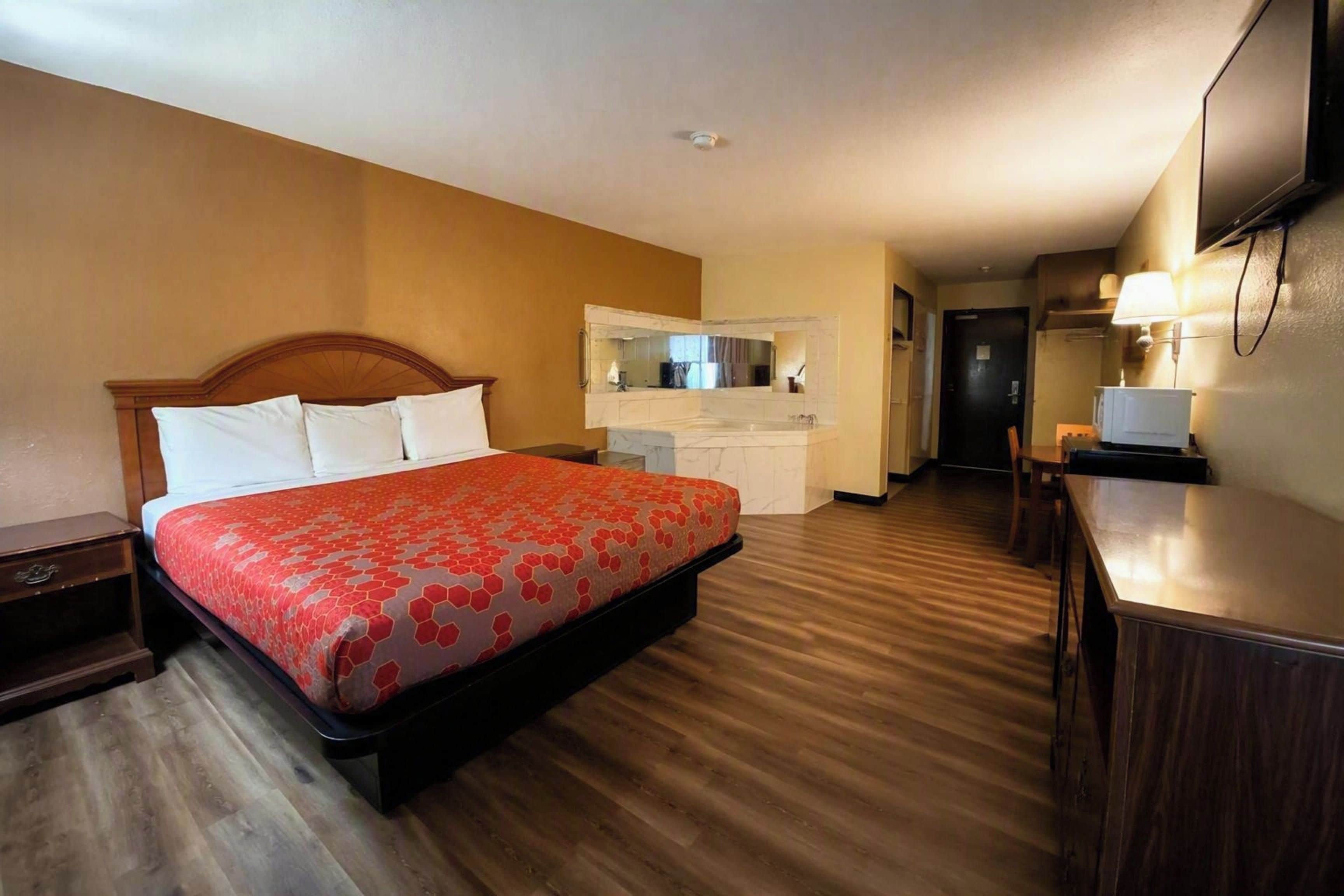 A hotel room with a bed, a desk, a mirror, and a kitchenette.
