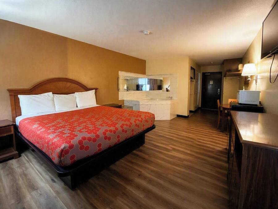Una habitación de hotel con cama, escritorio, espejo y kitchenette.