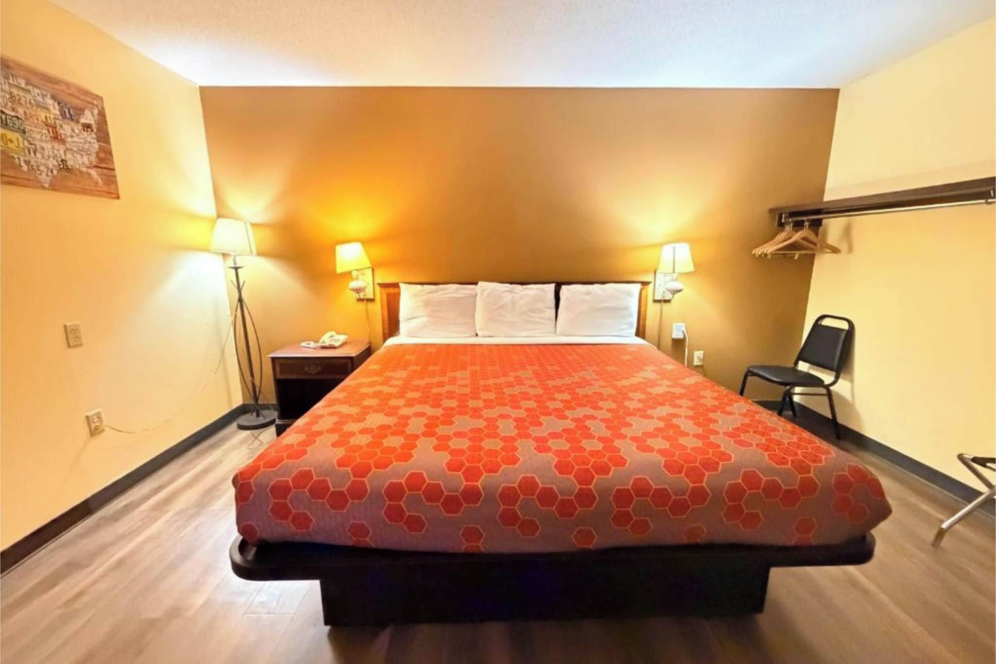 A hotel room with a bed, two bedside lamps, a nightstand, a chair, and a coat rack.