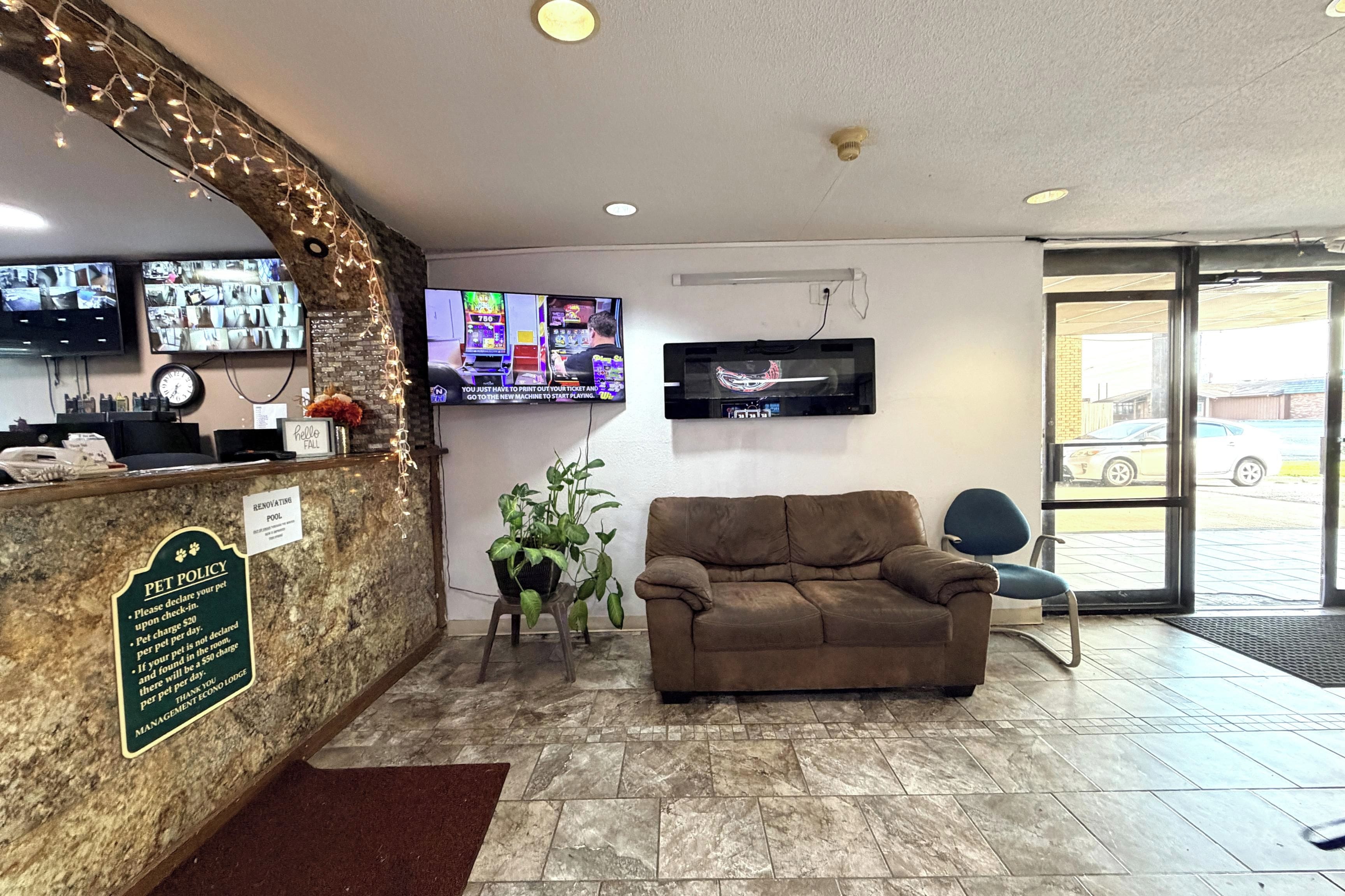 Un hall con mostrador de recepción, un televisor montado en la pared, un sofá y una planta en maceta.