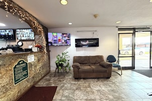 Un hall con mostrador de recepción, un televisor montado en la pared, un sofá y una planta en maceta.