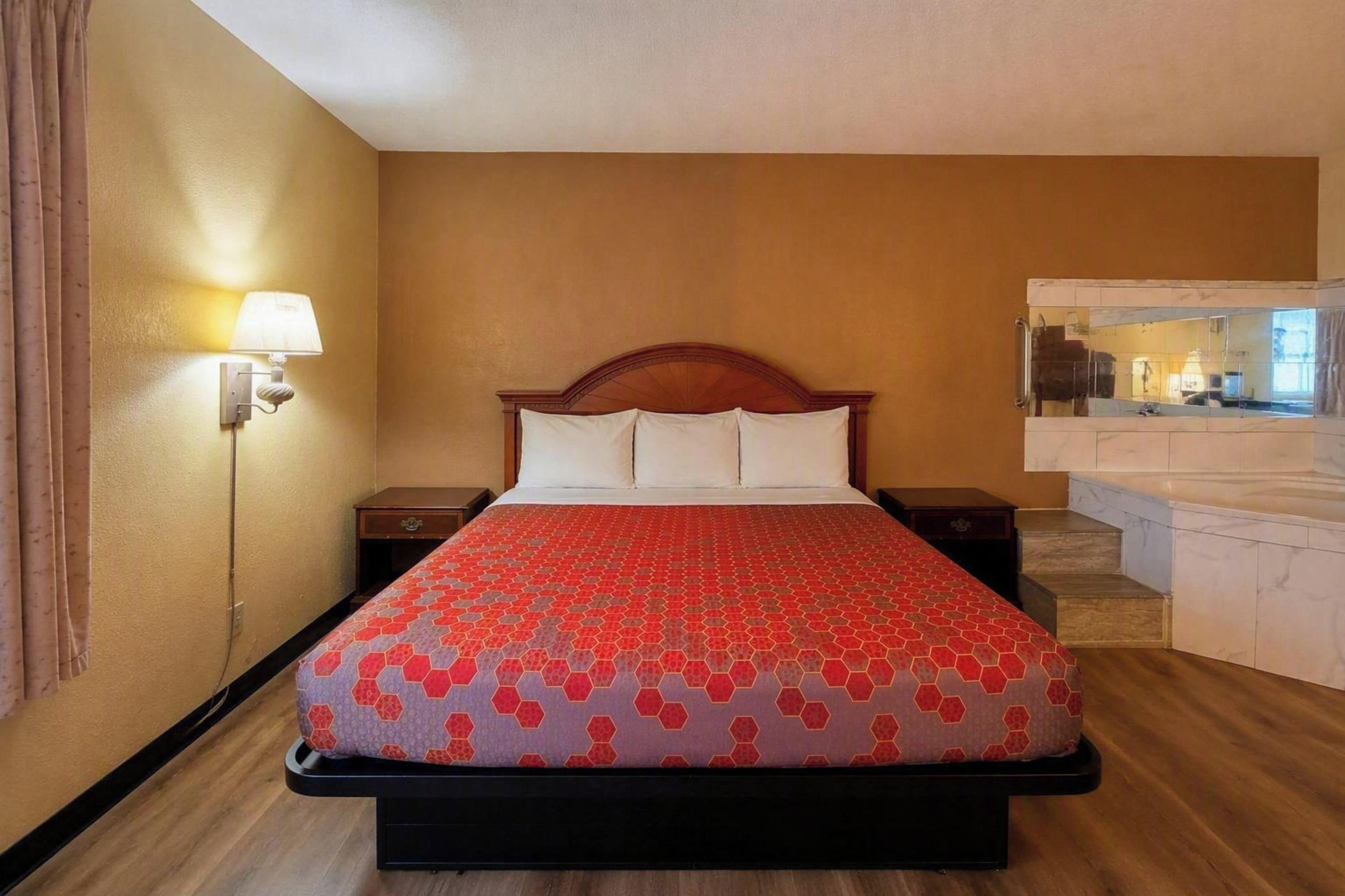A hotel room with a bed, a nightstand, a lamp, and a mirror.