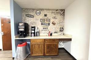 A coffee station with a coffee machine, a water bottle, and a trash bin.