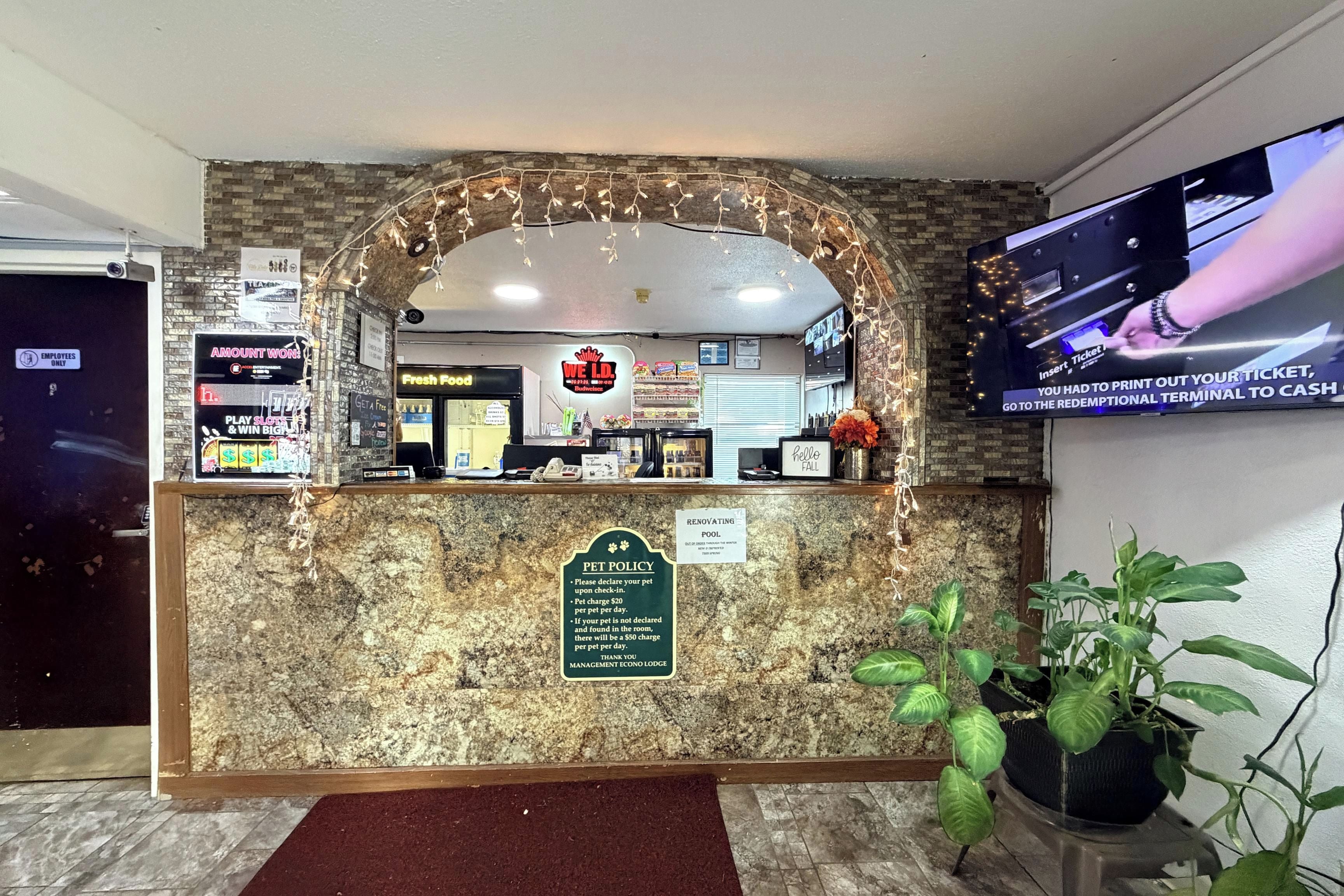 A hotel reception desk with a pet policy sign, a television screen, and a 'Fresh Food' sign.