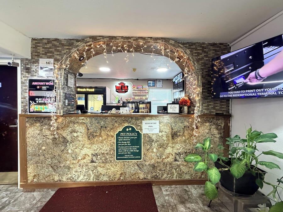 A hotel reception desk with a pet policy sign, a television screen, and a 'Fresh Food' sign.