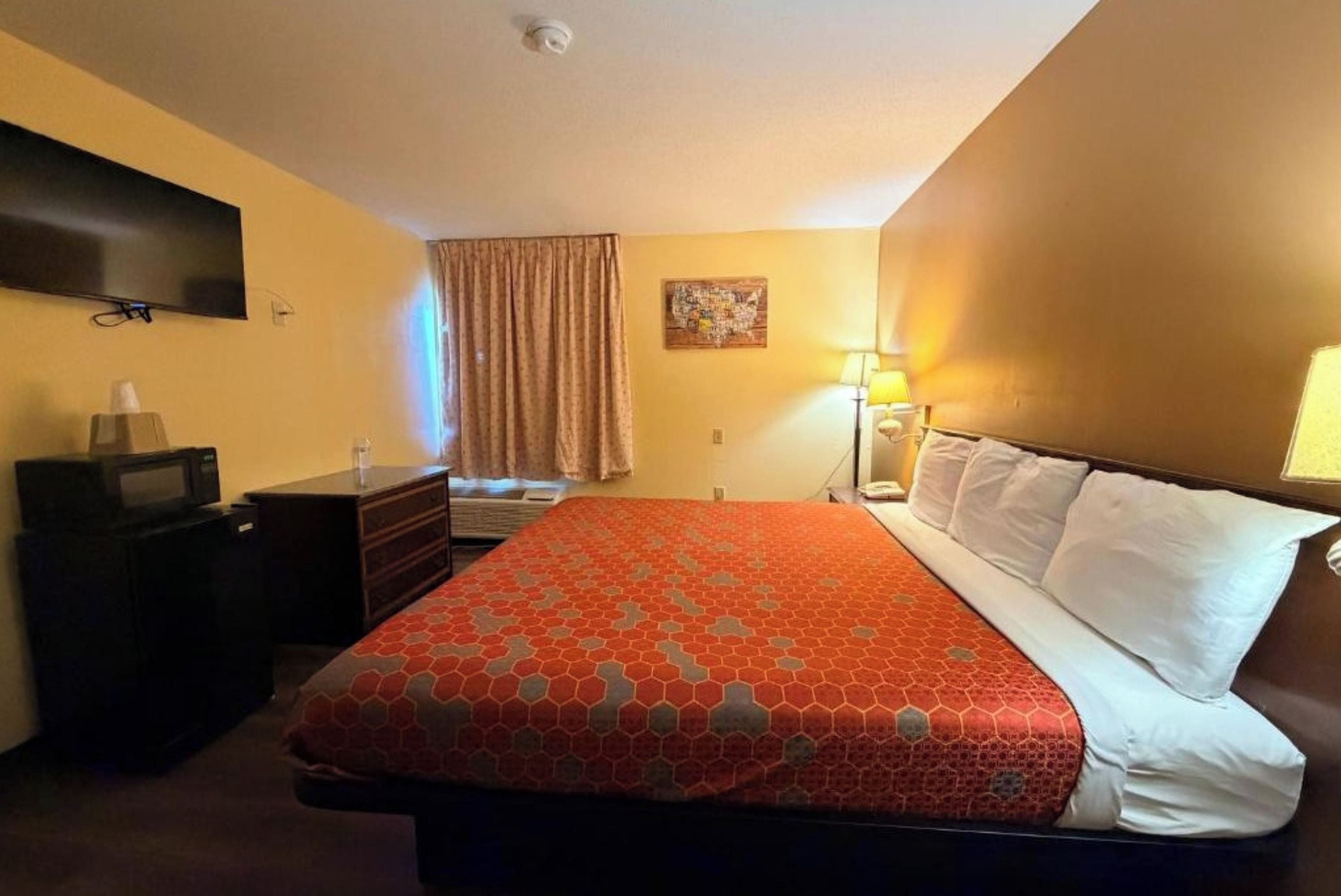 Una habitación de hotel con cama, escritorio, televisor y ventana con cortinas.