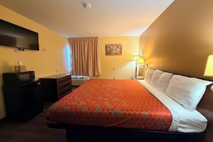 Una habitación de hotel con cama, escritorio, televisor y ventana con cortinas.