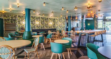 Un restaurante con mesas y sillas redondas, una zona de bar y una pared con diseño.