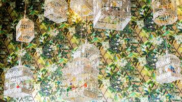 Multiple ornate birdcages hanging against a lattice wall with floral patterns.