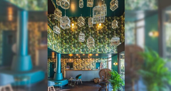 Un área de bar con una pared estampada en verde, jaulas de pájaros colgantes y asientos.