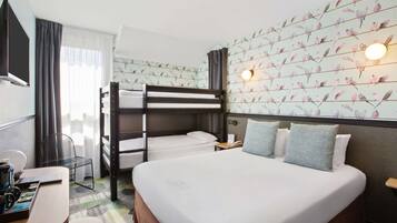 A hotel room with a bunk bed, a single bed, a desk with a chair, and a wall-mounted TV.