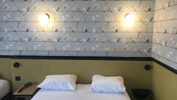 Habitación de hotel con una cama, dos almohadas blancas, una mesita de noche con un teléfono y una pared con estampado de pájaros.
