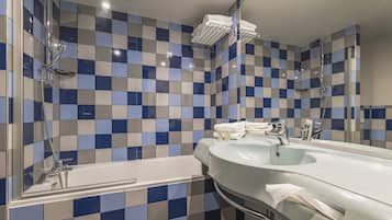 Un baño con pared de baldosas a cuadros, una bañera, un lavamanos y un espejo.