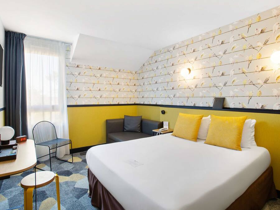 A hotel room with a large bed, a desk with a chair, a small table, and a TV.