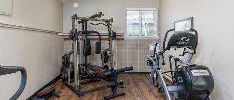 Een sportschool met een halterbank, een rek voor squats, een loopband en een elliptische trainer.