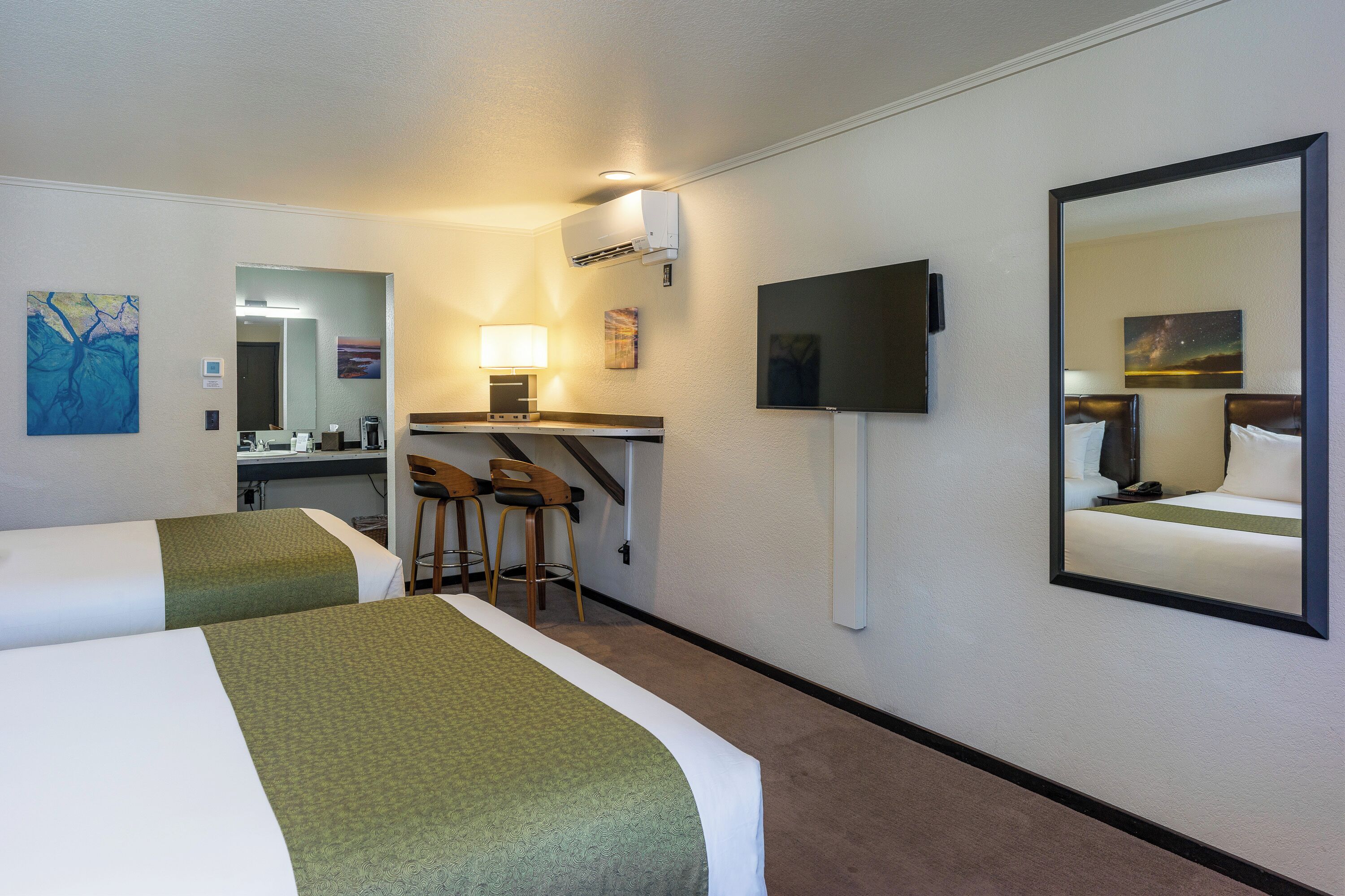 Een hotelkamer met twee bedden, een bureau met stoel, een televisie en een spiegel.