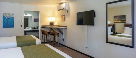 A hotel room with two beds, a desk with a chair, a TV, and a mirror.