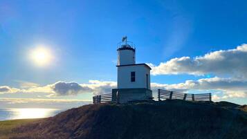 Un faro sobre una colina cubierta de hierba, con cielo despejado y el sol brillando.