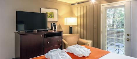 A hotel room with a bed, a TV, a desk with a lamp, and a chair.