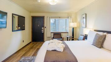 A hotel room with a large bed, a desk, a chair, a window with curtains, and a door.