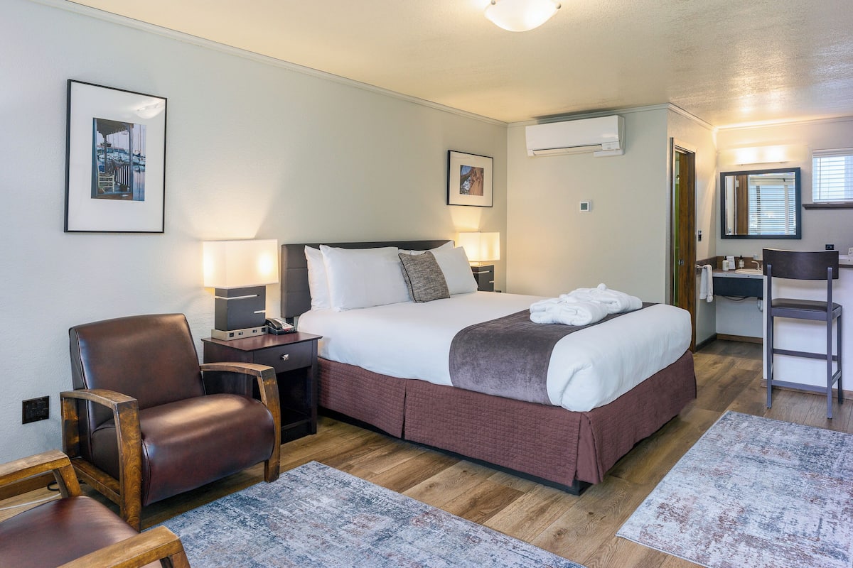 A neatly arranged bedroom with a large bed, a chair, a desk, and a mirror.
