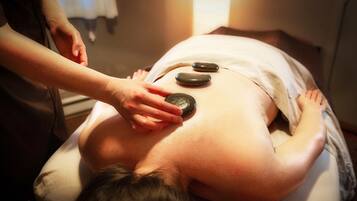 A massage therapy session with a person lying face down on a massage table, receiving pressure from a therapist's hands and stones.