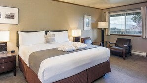 A hotel room with a large bed, two bedside tables, a chair, and a window with curtains.