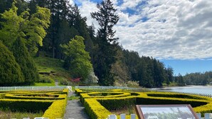 A landscaped garden with neatly trimmed hedges, a white picket fence, and a wooden signboard. - Earthbox Inn & Spa (Friday Harbor)