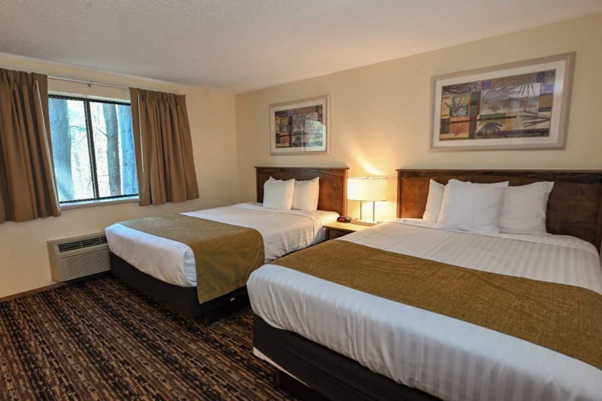 A hotel room with two beds, a window with curtains, a radiator, and two framed pictures on the wall.