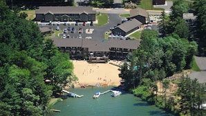 Vista aérea de um resort com praia, um cais com barcos e uma área de estacionamento.
