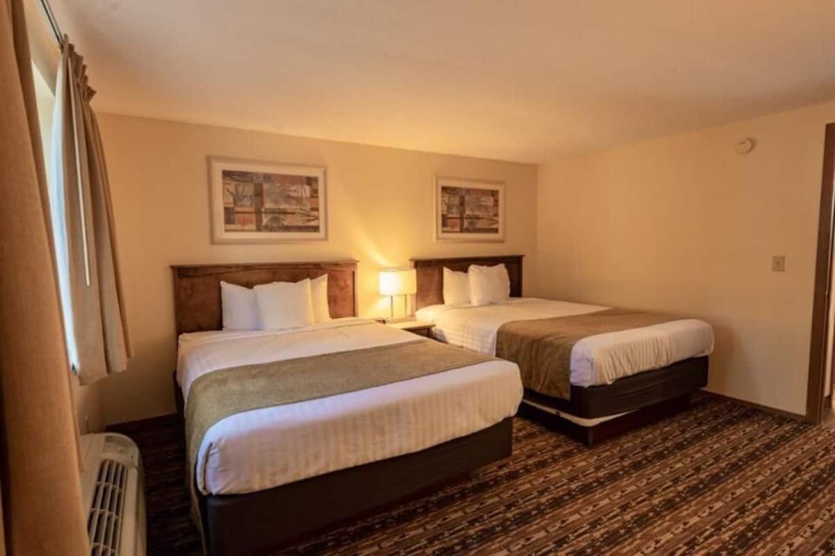 A hotel room with two beds, a heater, and two wall-mounted lamps.