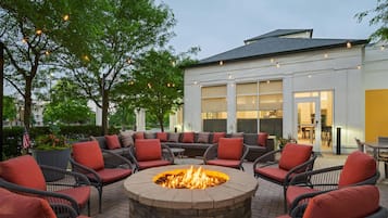 An outdoor seating area with a fire pit, wicker furniture, and a building with large windows in the background.