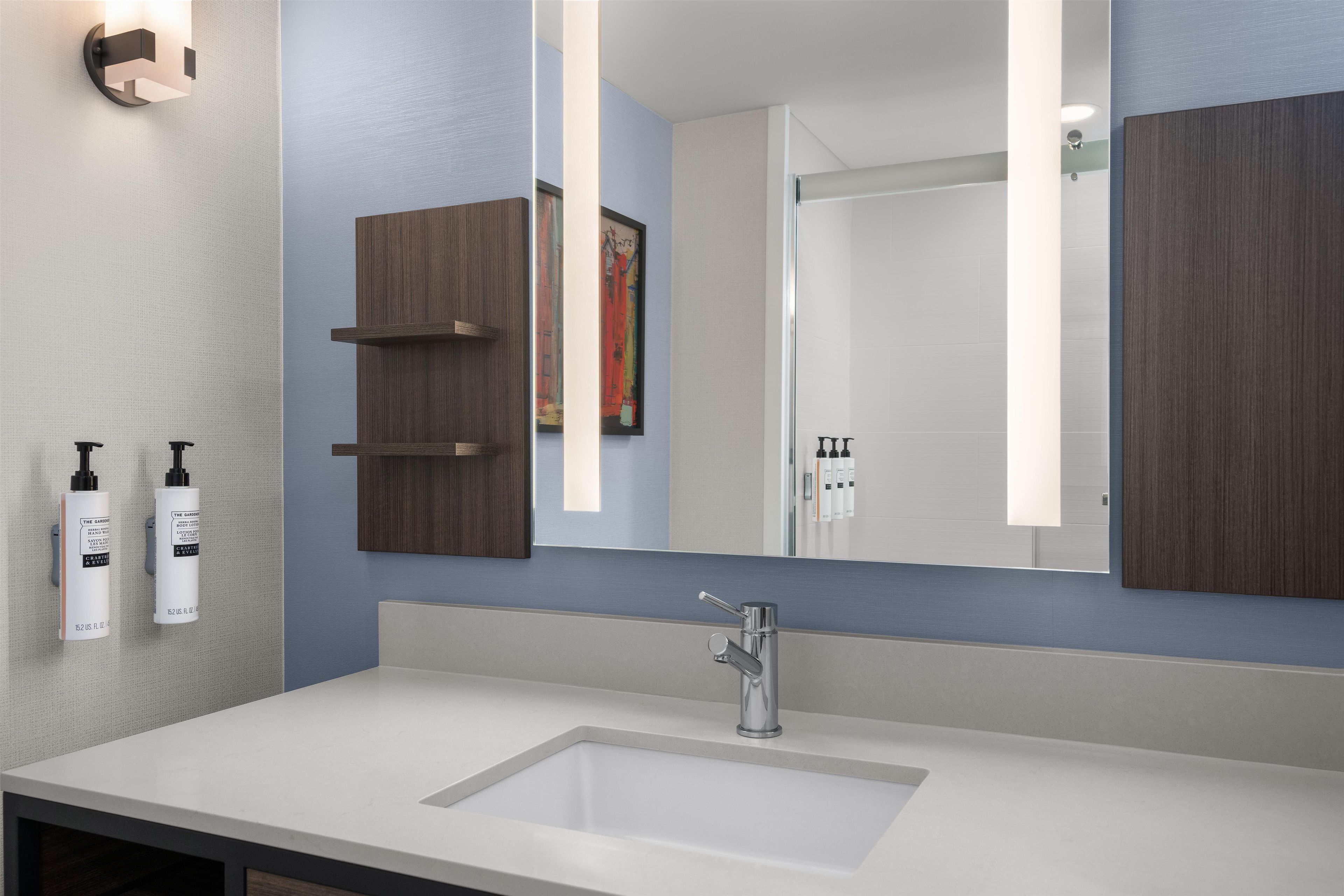 A modern bathroom with a large mirror, a white sink, and two wooden cabinets.